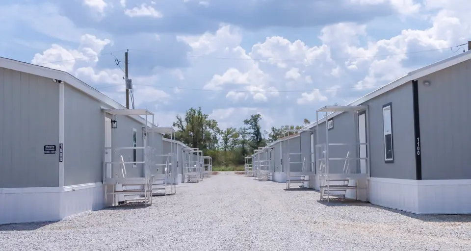 Two rows of gray accommodation units with covered entry stairs facing a gravel lane