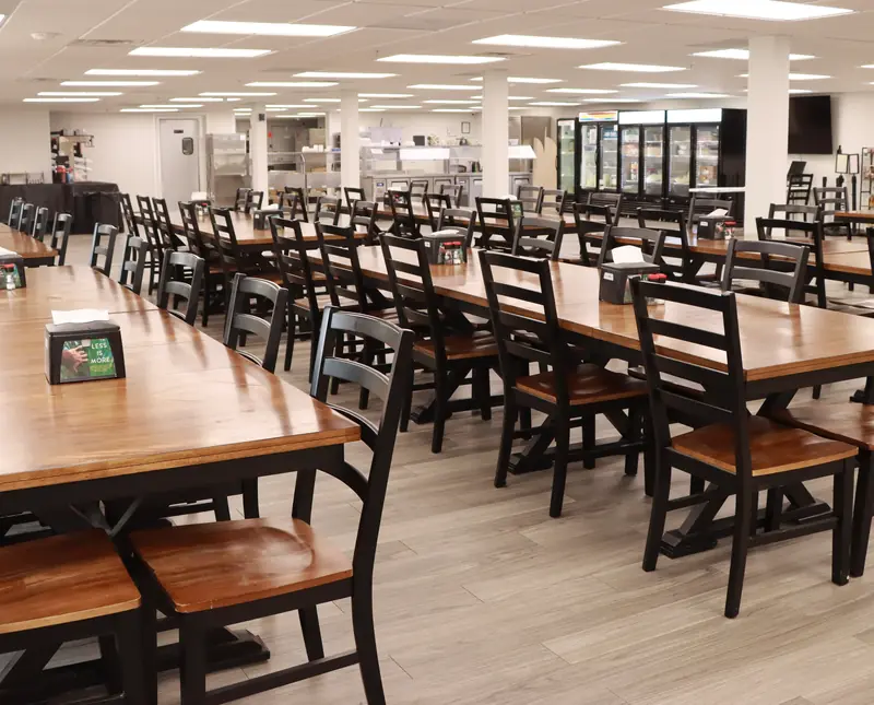 Dining hall with wood-top tables, black chairs and glass-door coolers