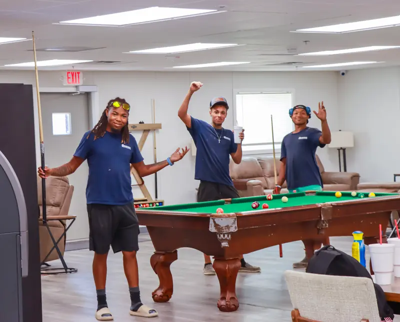 Three people standing around a green pool table in a recreation room