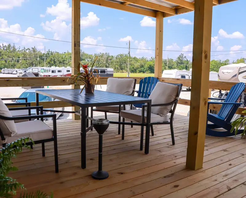 Table and chairs on a covered wooden porch, with RVs visible beyond the railing